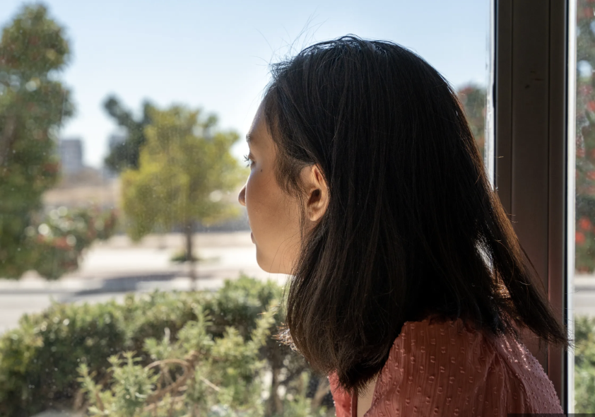 Woman reflecting by a sunlit window, thinking about her repeating relationship patterns